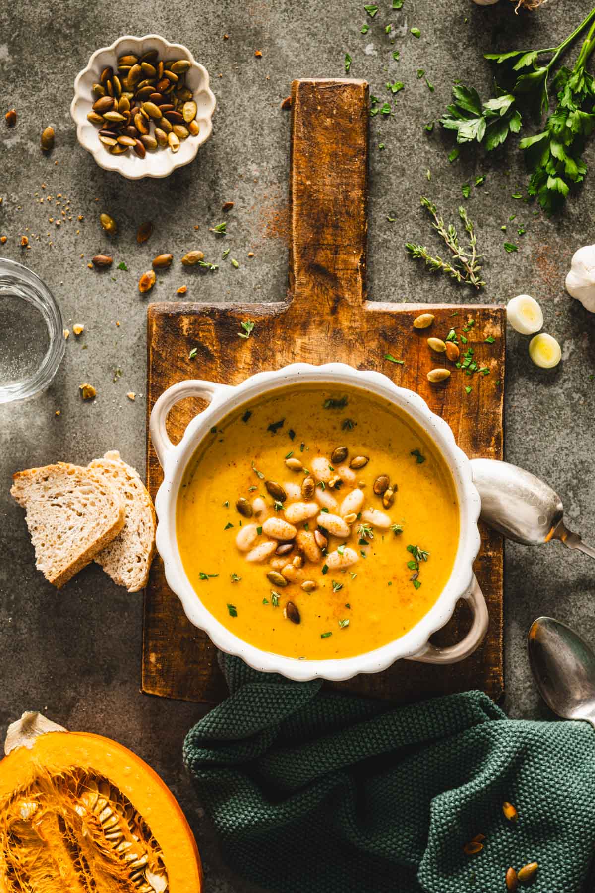 bowl with pumpkin soup on a wooden board, green background, half of a fresh pumpkin, spoons