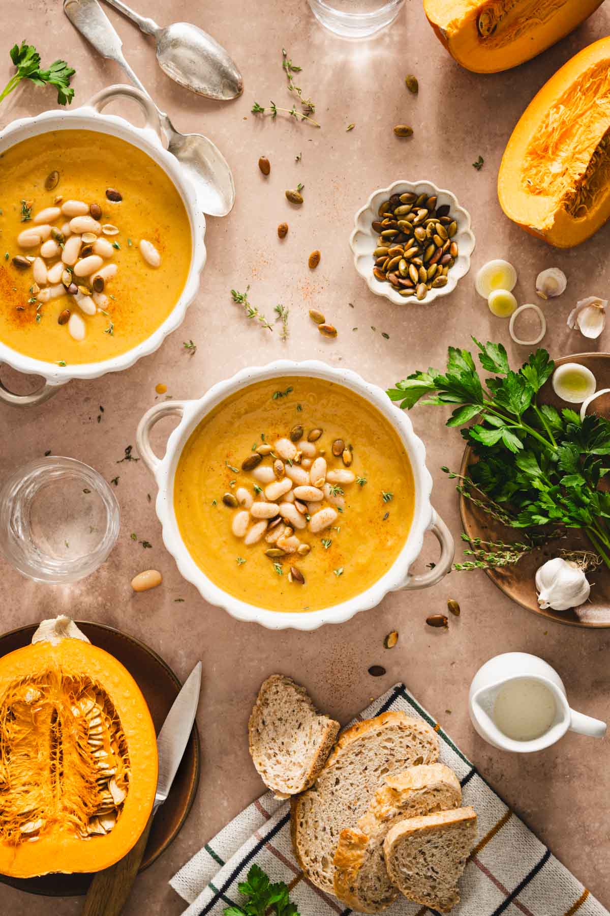 pumpkin soup in serving bowls, fresh parsley, cut up pumpkin, bread slices