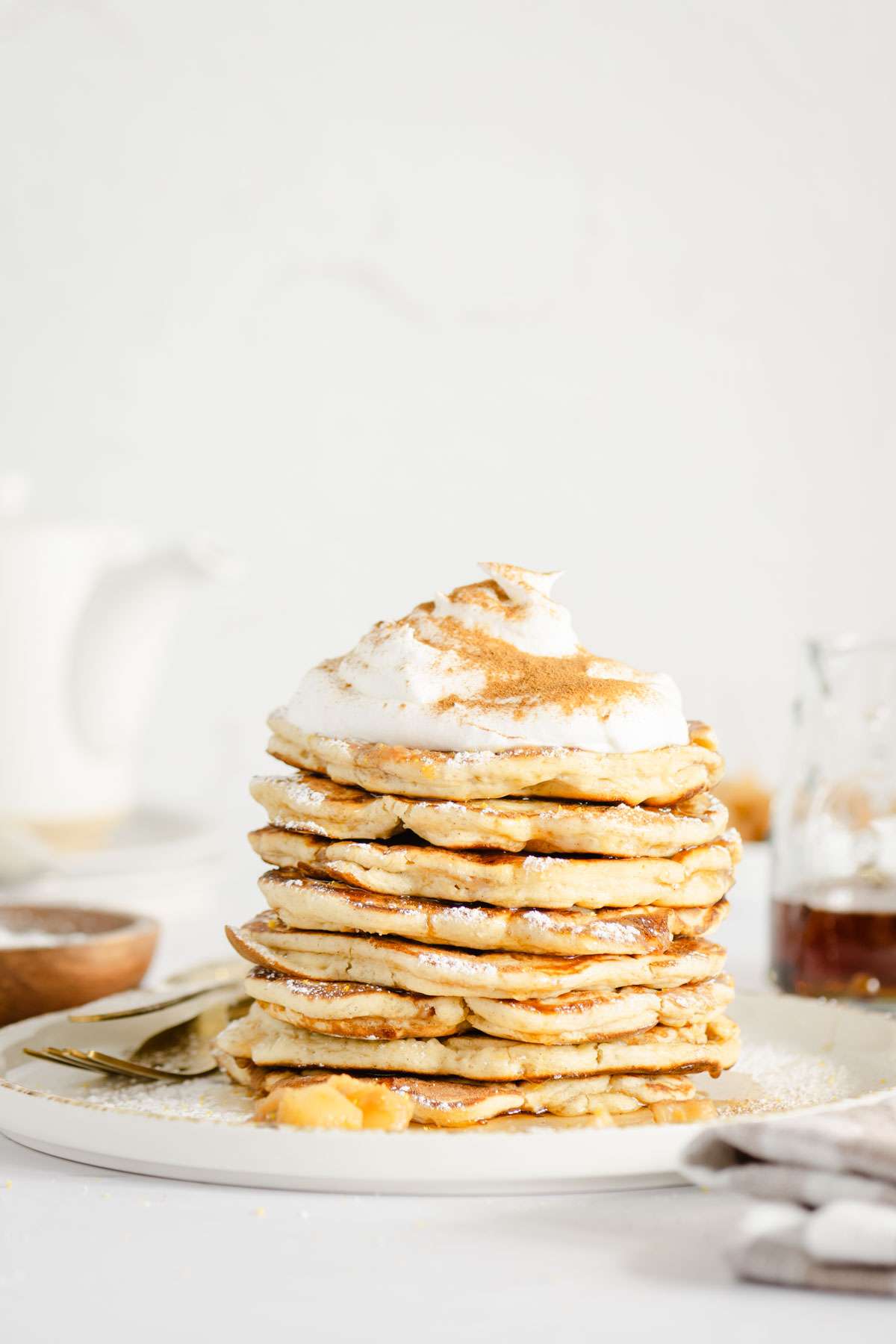 front view of stack of racuchy with whipped topping, kettle, plates in the back