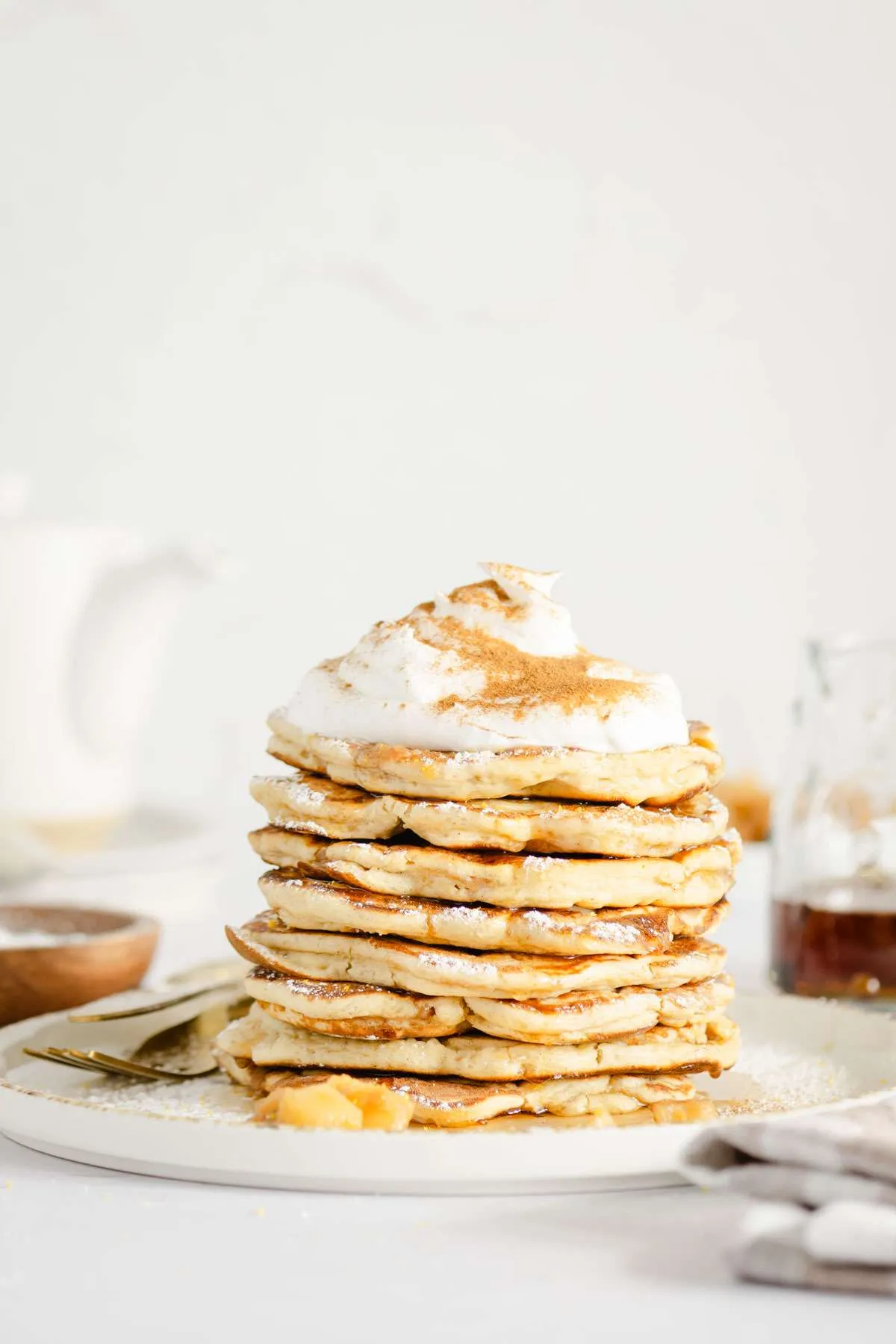 front view of stack of racuchy with whipped topping, kettle, plates in the back