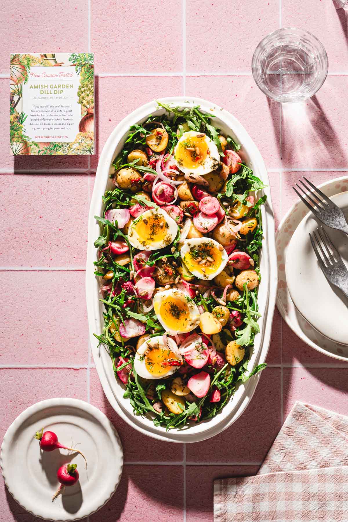 serving platter with the salad, dish with th edressing, plates, glasses with water, brand pacakge