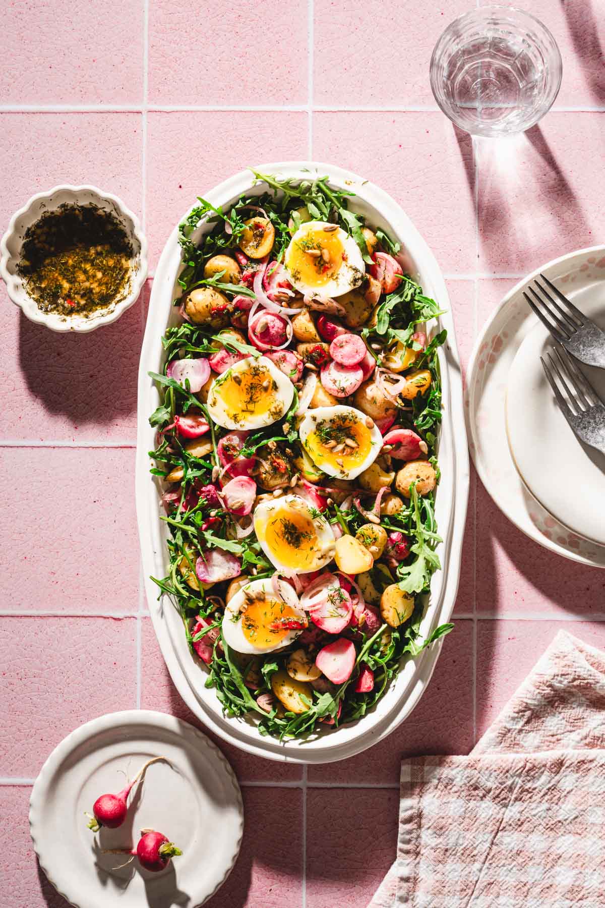 serving platter with the salad, dish with th edressing, plates, glasses with water