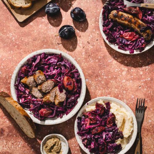 red cabbage on serving plates, sausage, bread, plums