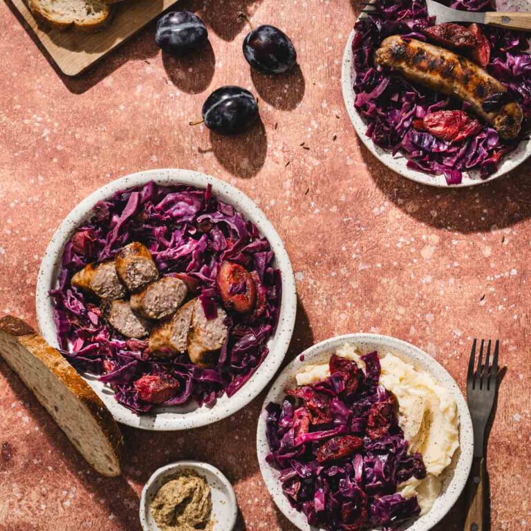 red cabbage on serving plates, sausage, bread, plums