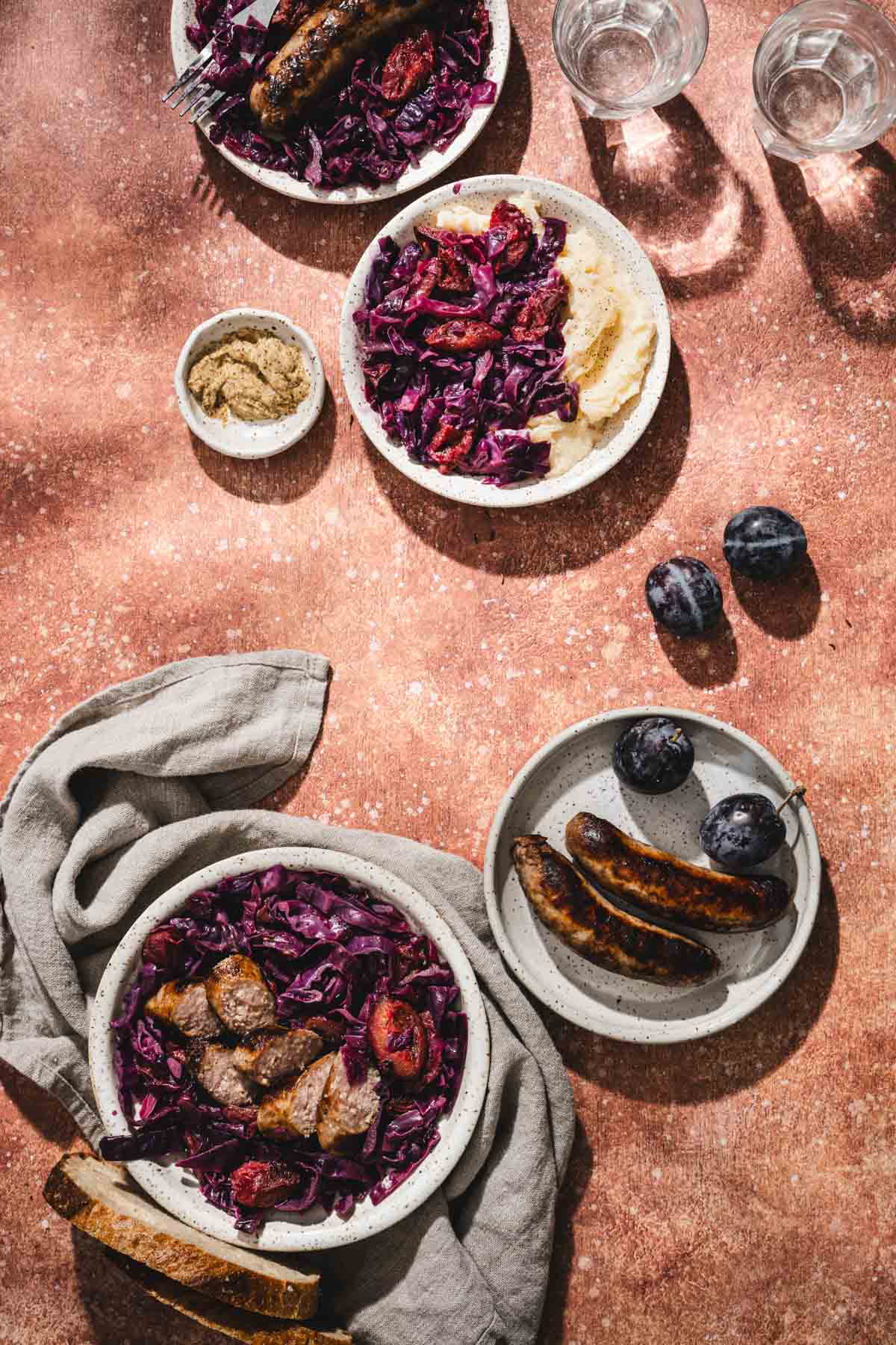 various plates with red cabbage , glasses with water, plums, napkin