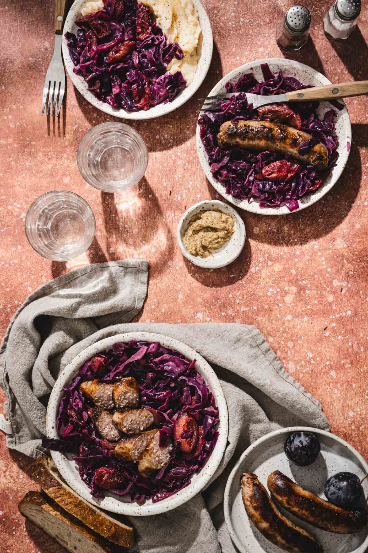 various plates with red cabbage , glasses with water, plums