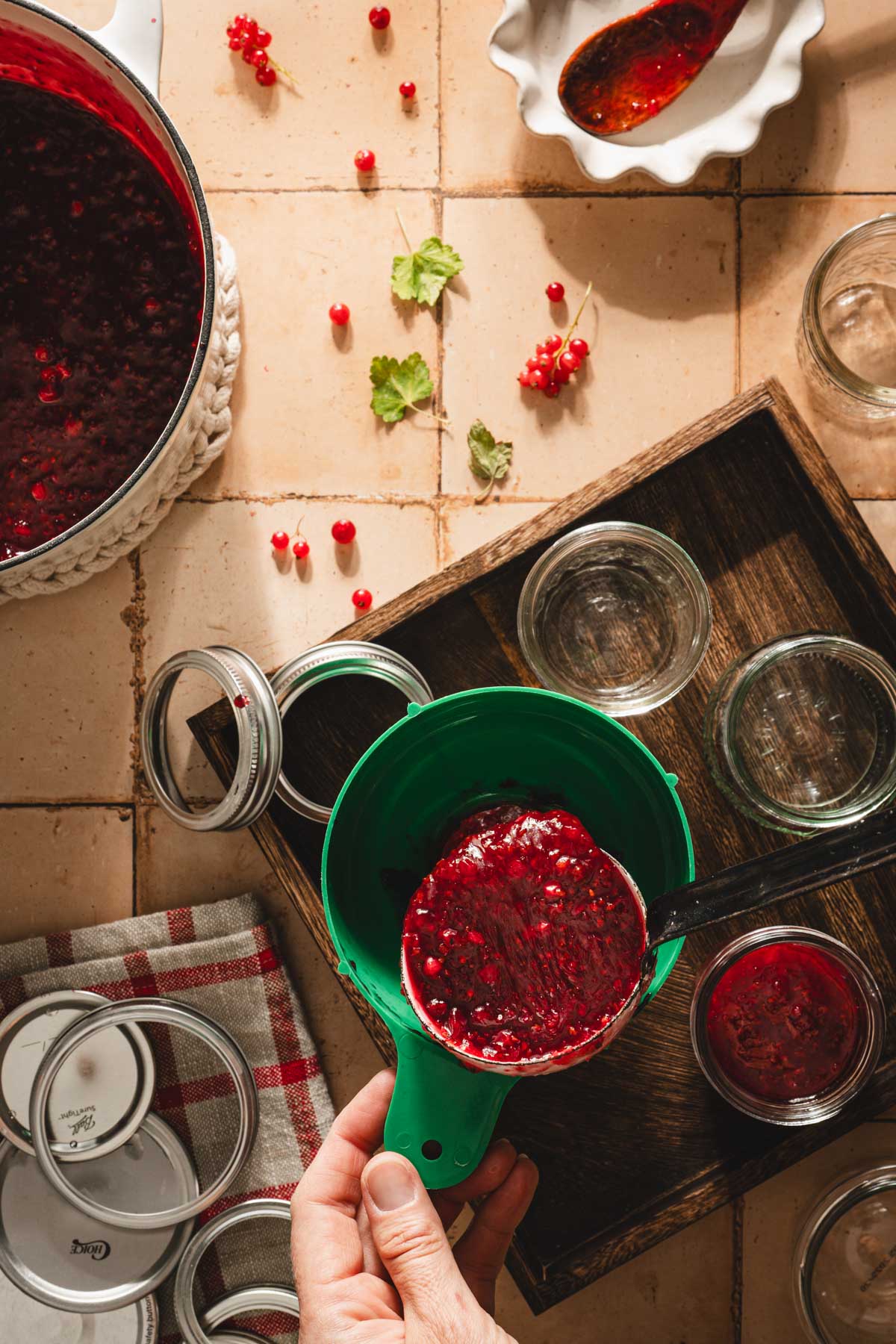 hands in frame holding funnel over jars with jam