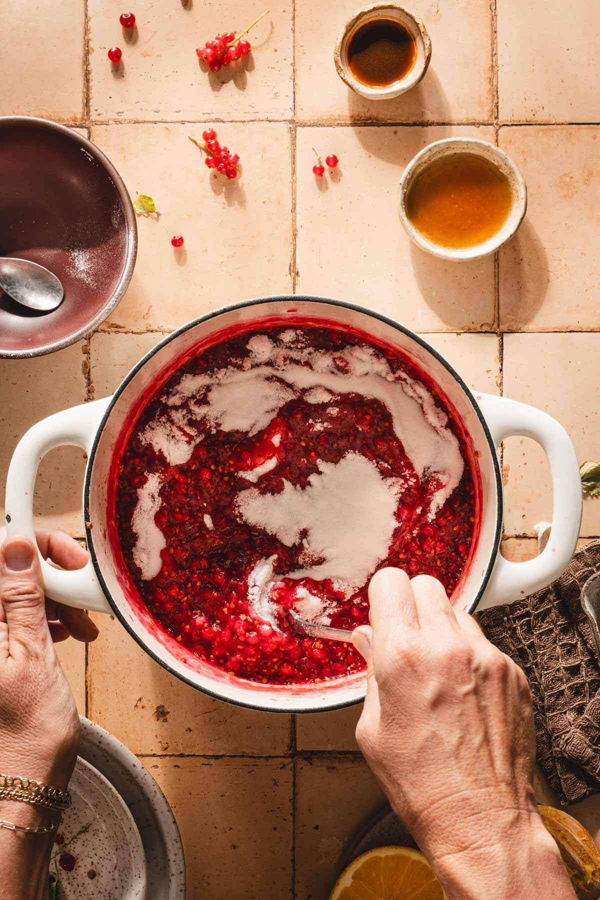 hands in frame stirring sugar into the jam