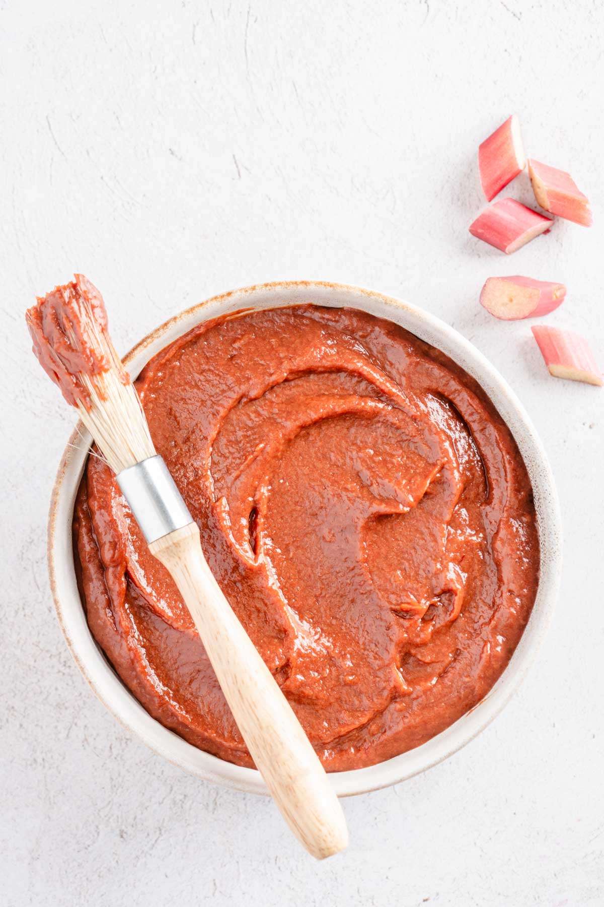 rhubarb BBQ sauce in a glass bowl, bbq brush, few pieces of rhubarb