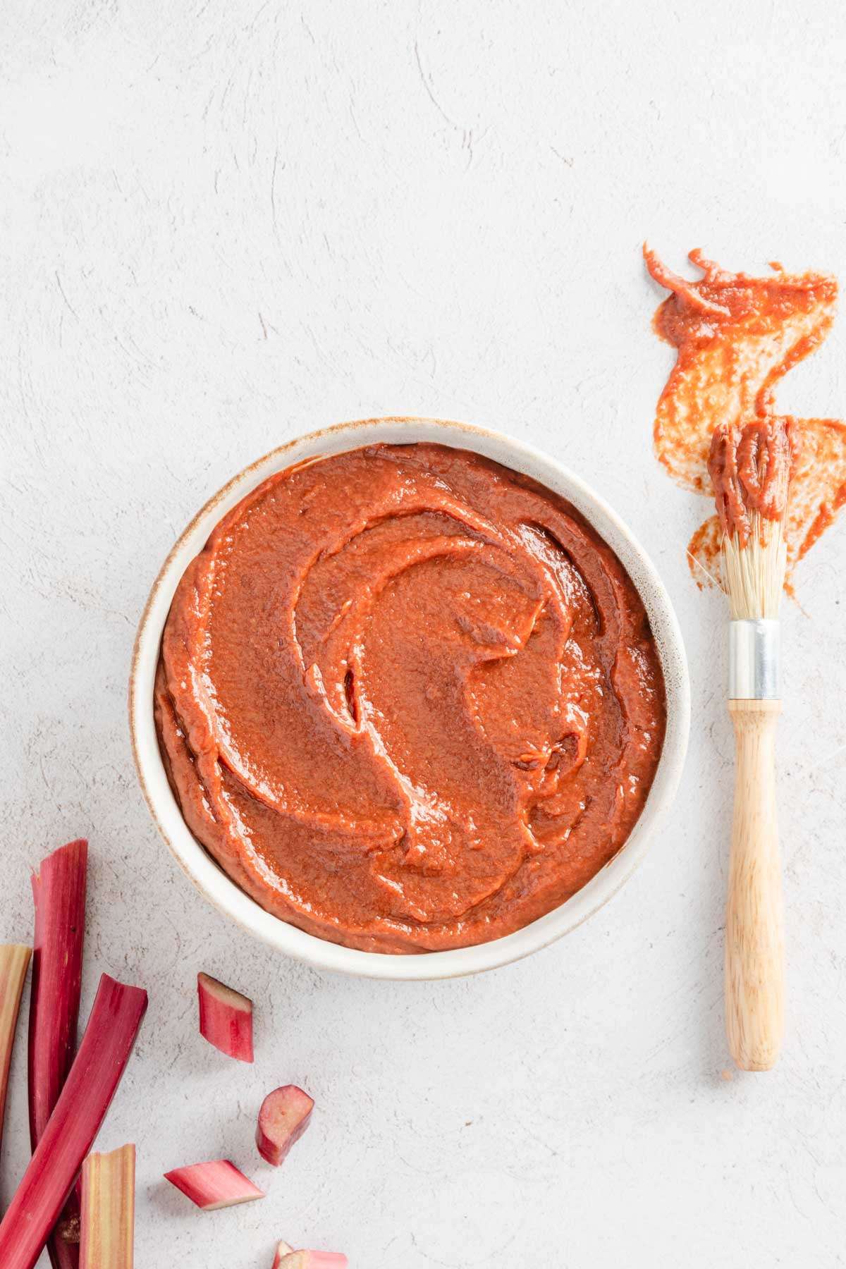 rhubarb BBQ sauce in a glass bowl, bbq brush, few pieces of rhubarb