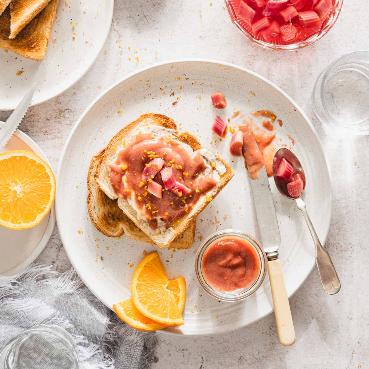 toast with rhubarb butter on it, dish with compote, spoon, knife, orange slices