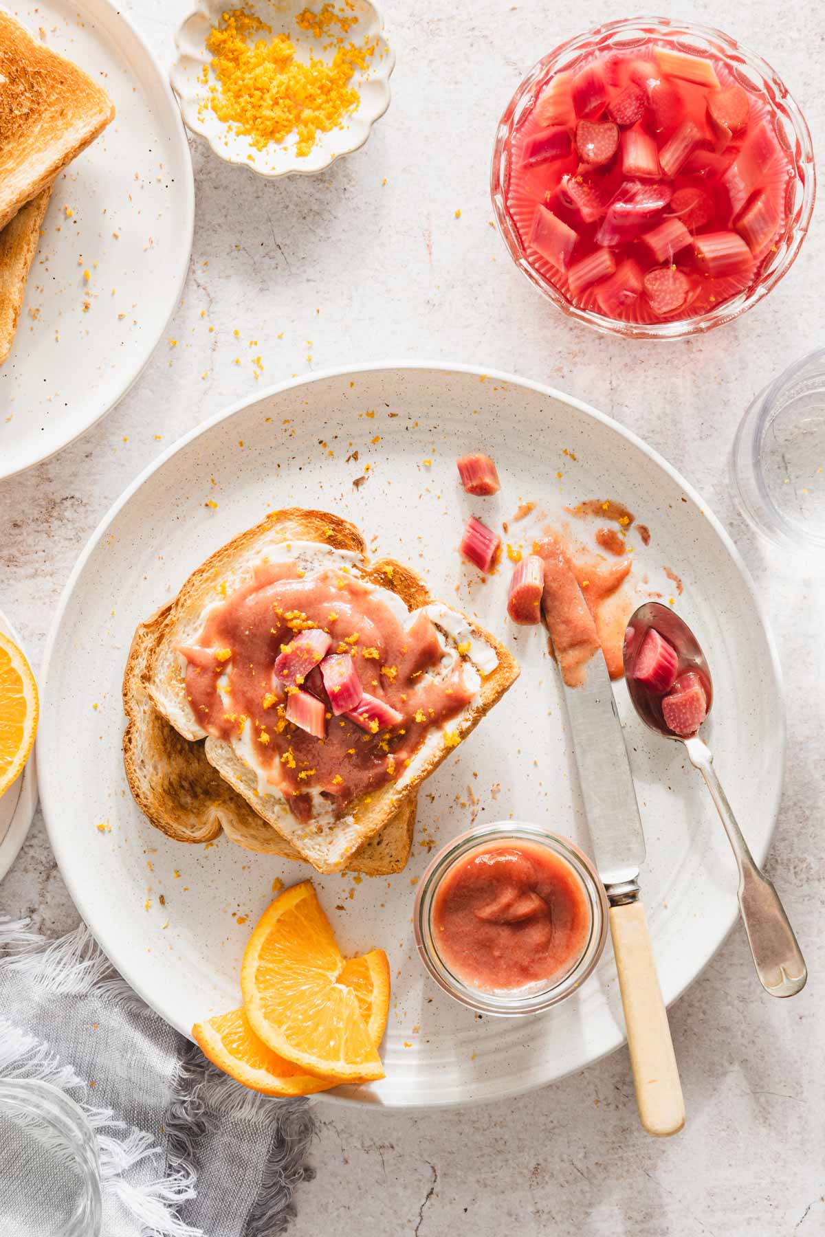 toast with rhubarb butter on it, dish with compote, spoon, knife, orange slices