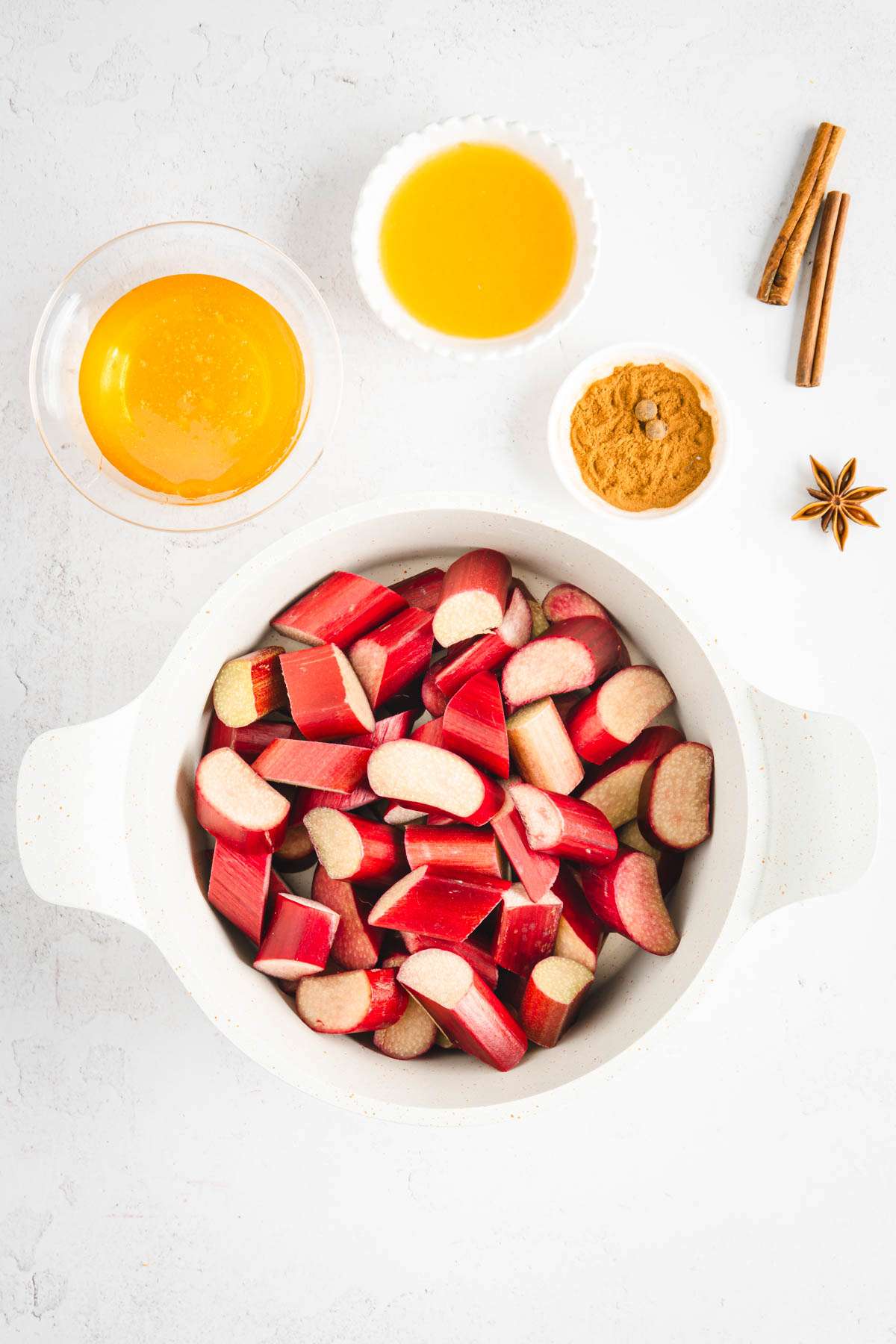 cut up rhubarb in a sauce pan, small dishes with other ingredients around