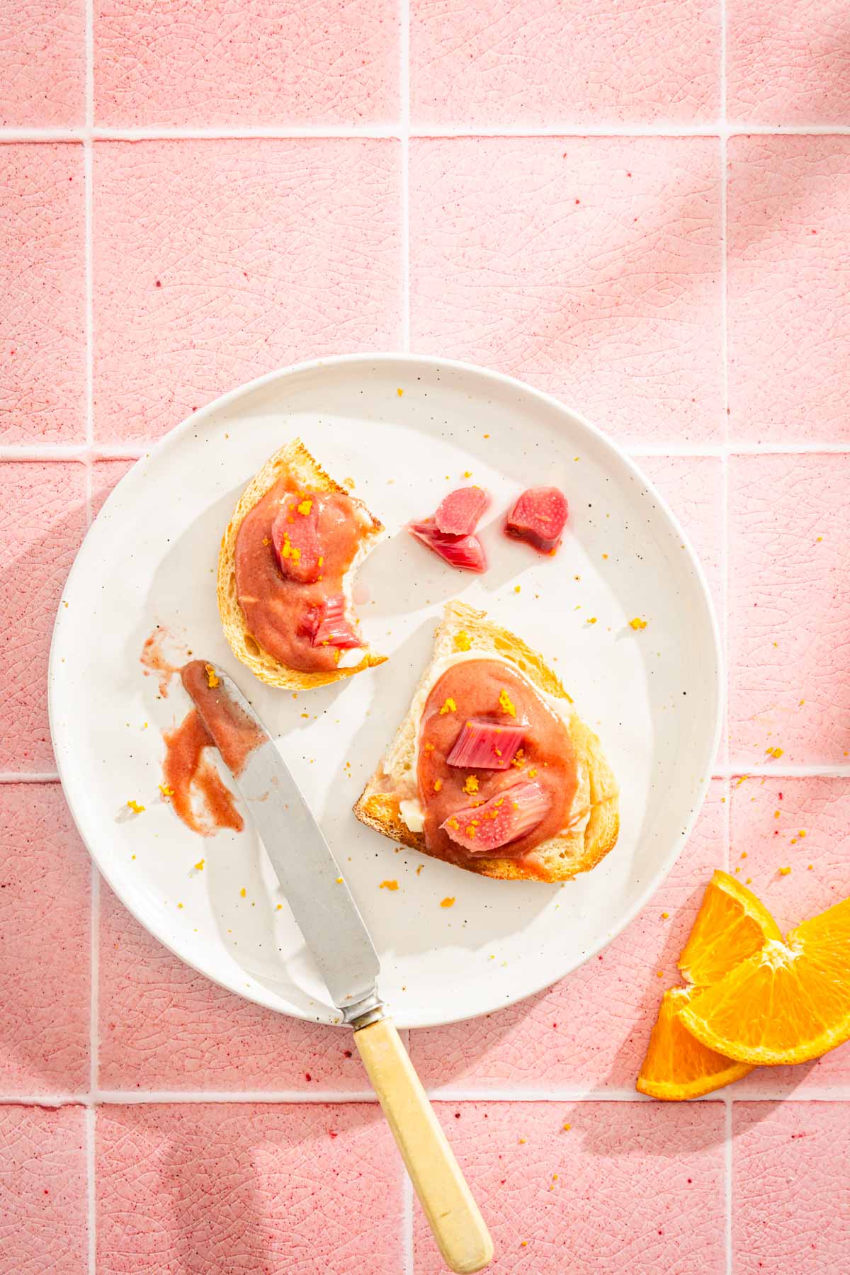 toast with rhubarb butter on a a plate, orange zest and slices, knife