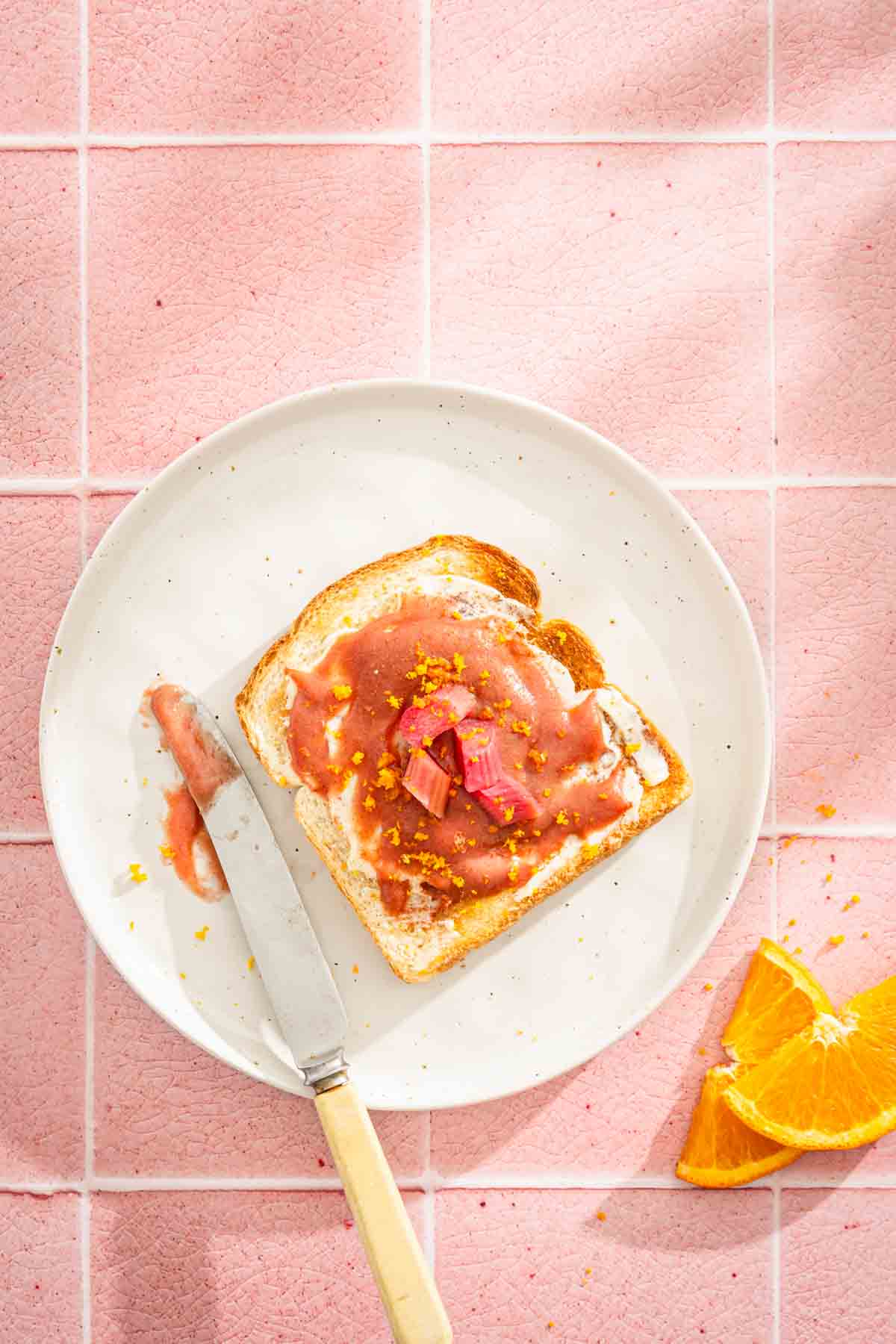 toast with rhubarb butter on a a plate, orange zest and slices, knife