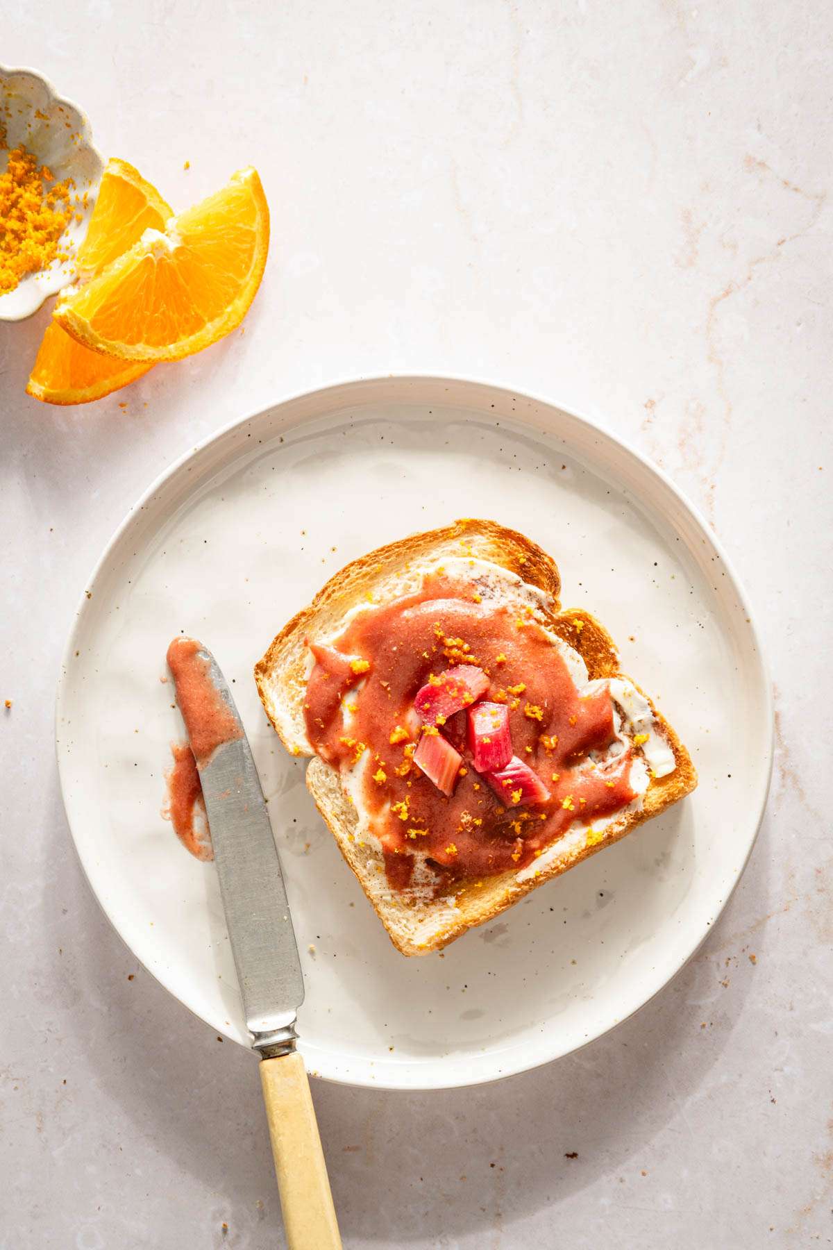 toast with rhubarb butter on a a plate, orange zest and slices, knife