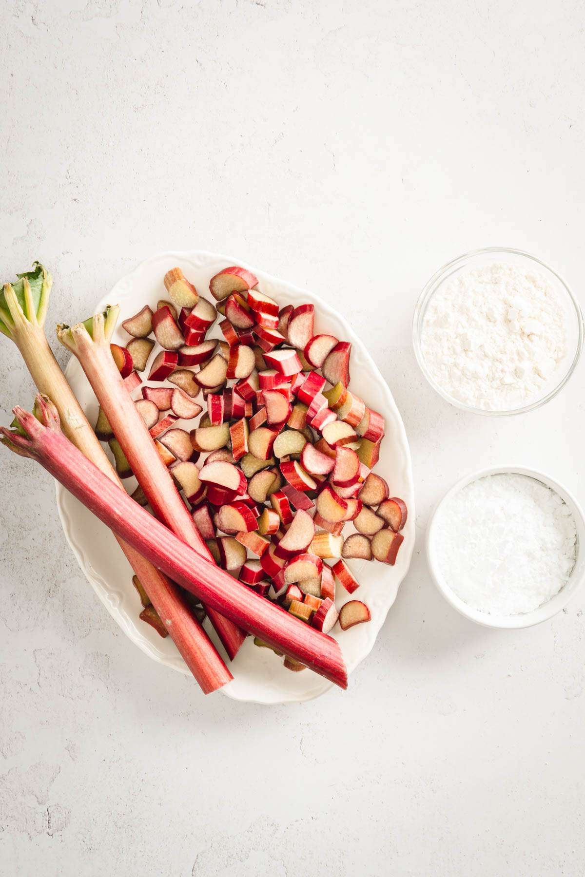 cut up rhubarb on a serving plate, dish with flour and another with powdered sugar