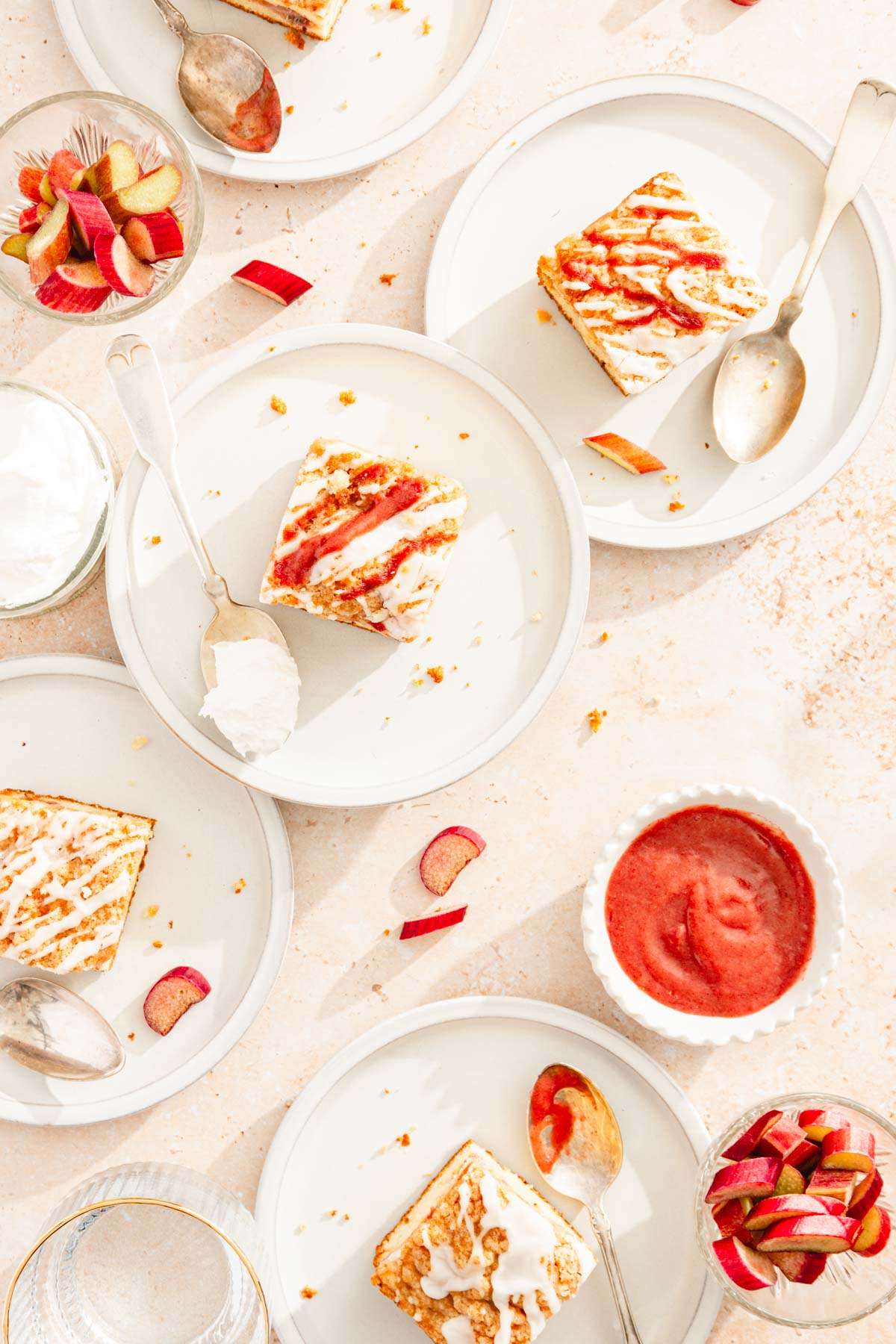 top view, slices of rhubarb cake on various plates, spoons and a dish with rhubarb butter