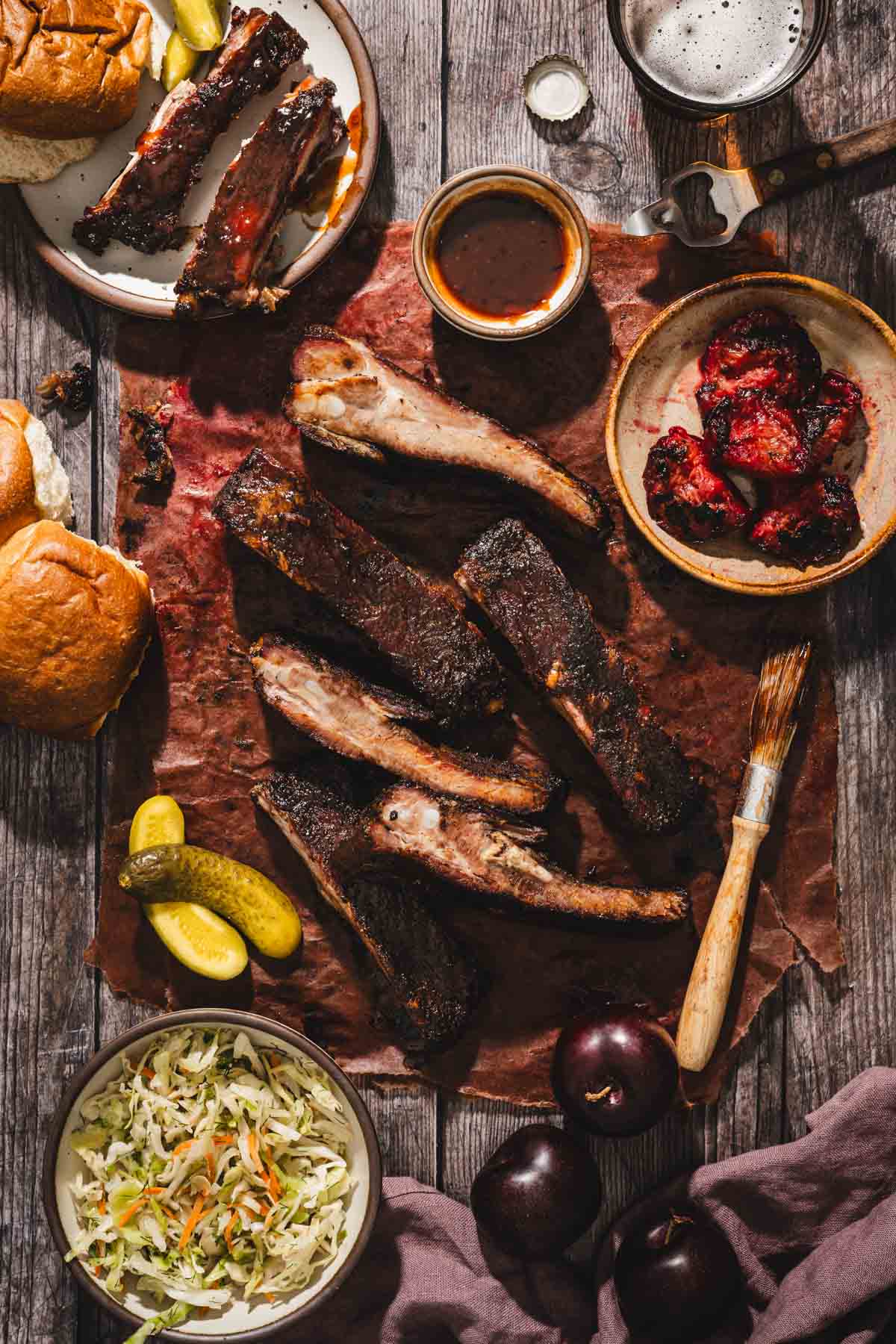 smoked,c ut up ribs on a butcher paper, several dishes with salads, bbq sauce, buns