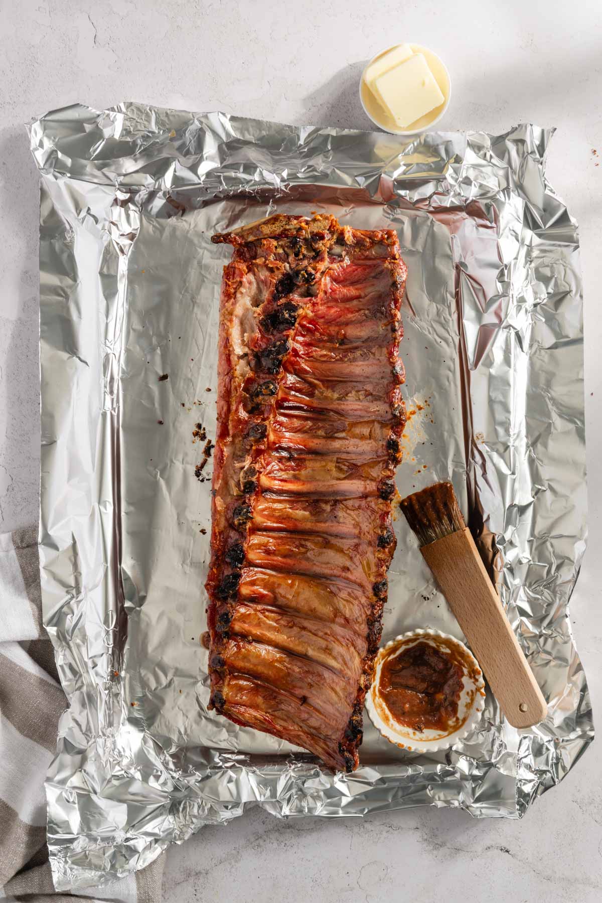 Smoked pork ribs on a foil, small dish with bbq sauce, bbq brush