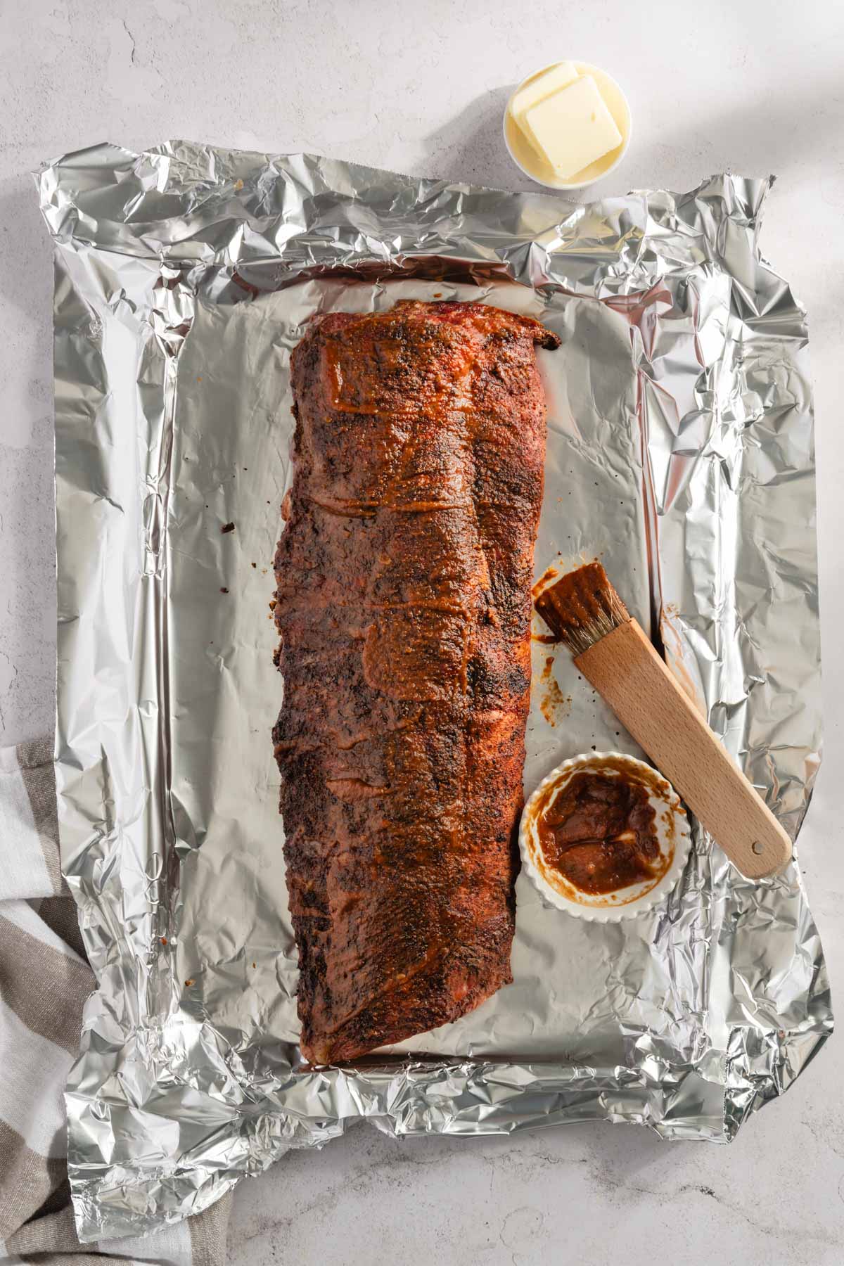 Smoked pork ribs on a foil, small dish with bbq sauce, bbq brush