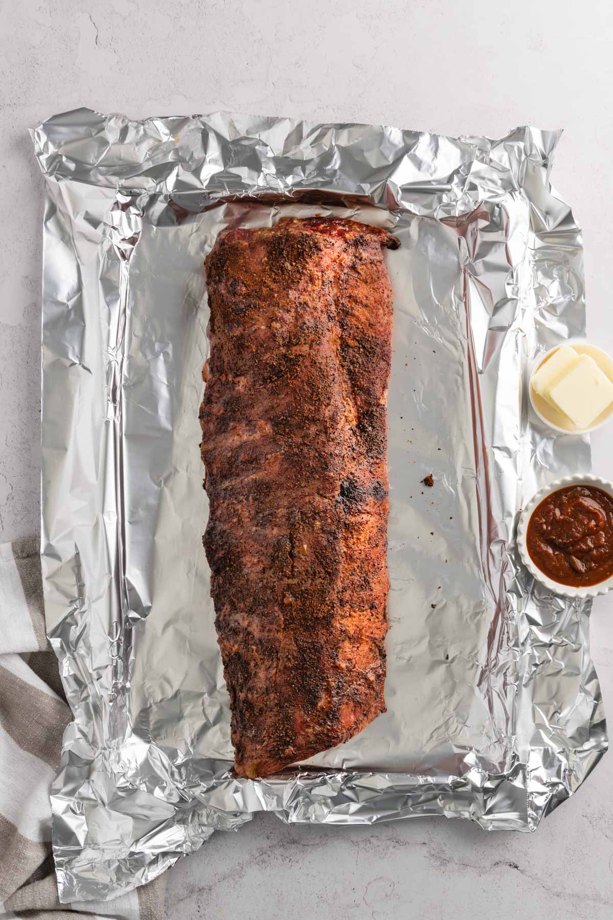 Smoked pork ribs on a foil, small dish with butter and bbq sauce