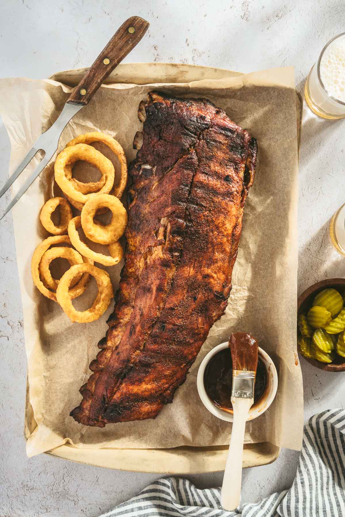 smoked ribs, cut into pieces, glass with beer, pickles, dish with bbq sauce