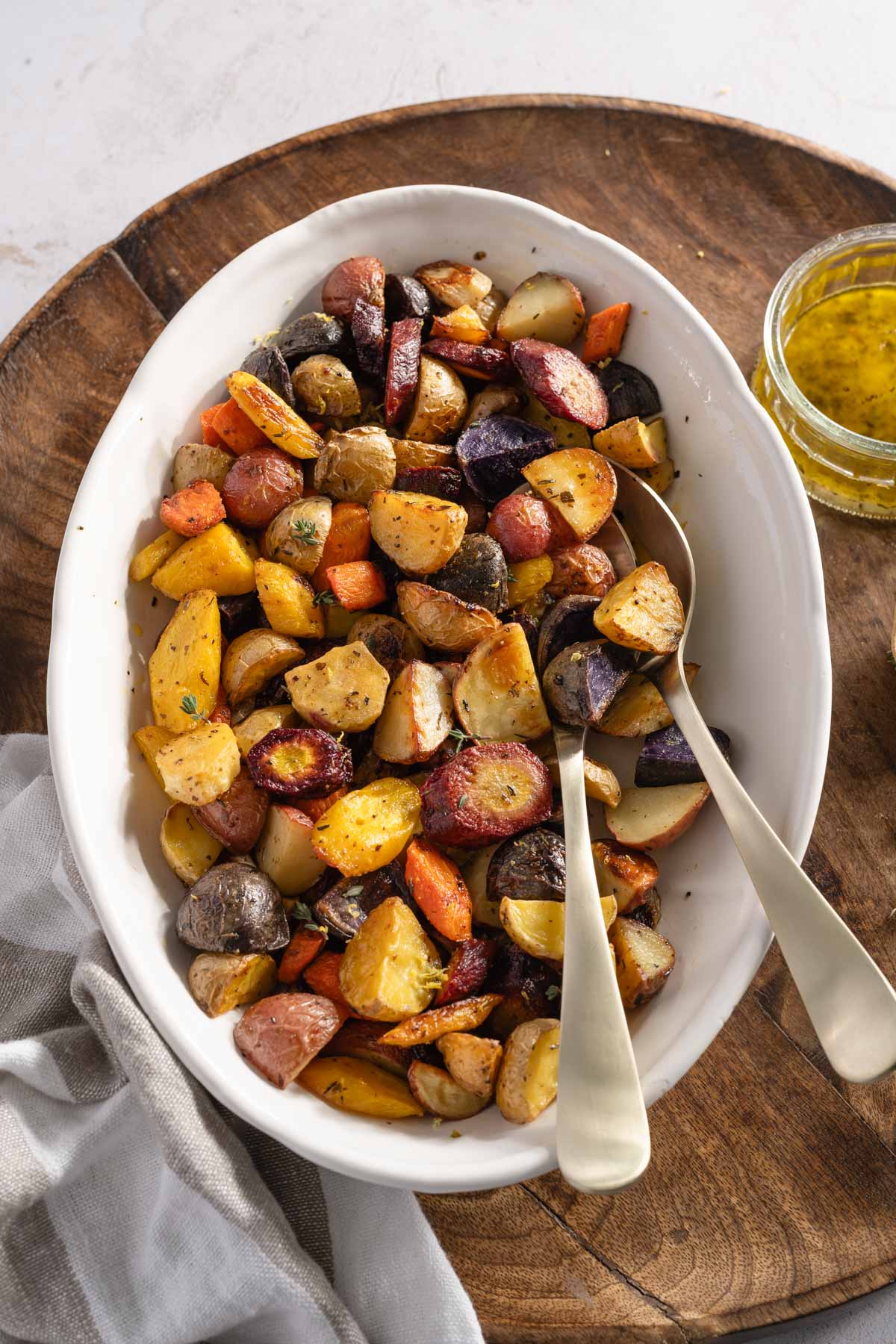 roasted veggies in a glass dish, two serving spoons, small dish with dressing