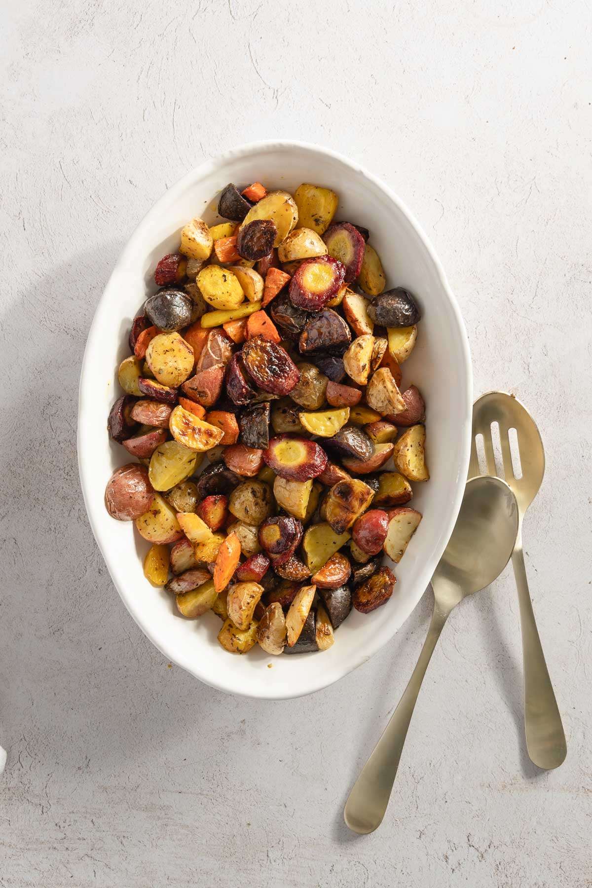 Roasted Vegetables in a glass dish, two serving spoons on the sinde