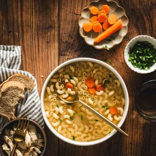 rosol in a serving bowl, sliced carrots on a small plate, parsley in a small bowl, shredded chicken on a plate