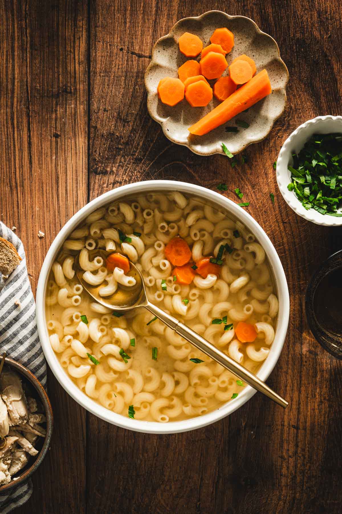 rosol in a serving bowl, sliced carrots on a small plate, parsley in a small bowl, shredded chicken on a plate