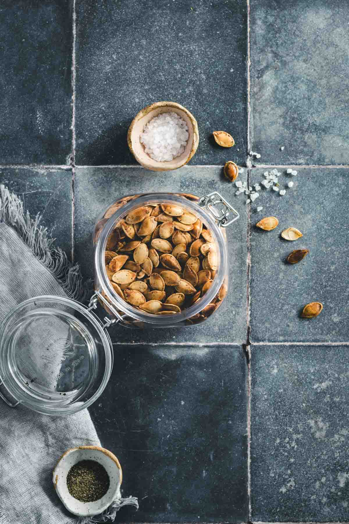 ROASTED PUMPKIN SEEDS IN A GLASS JAR; BLUE TILE BACKGROUND