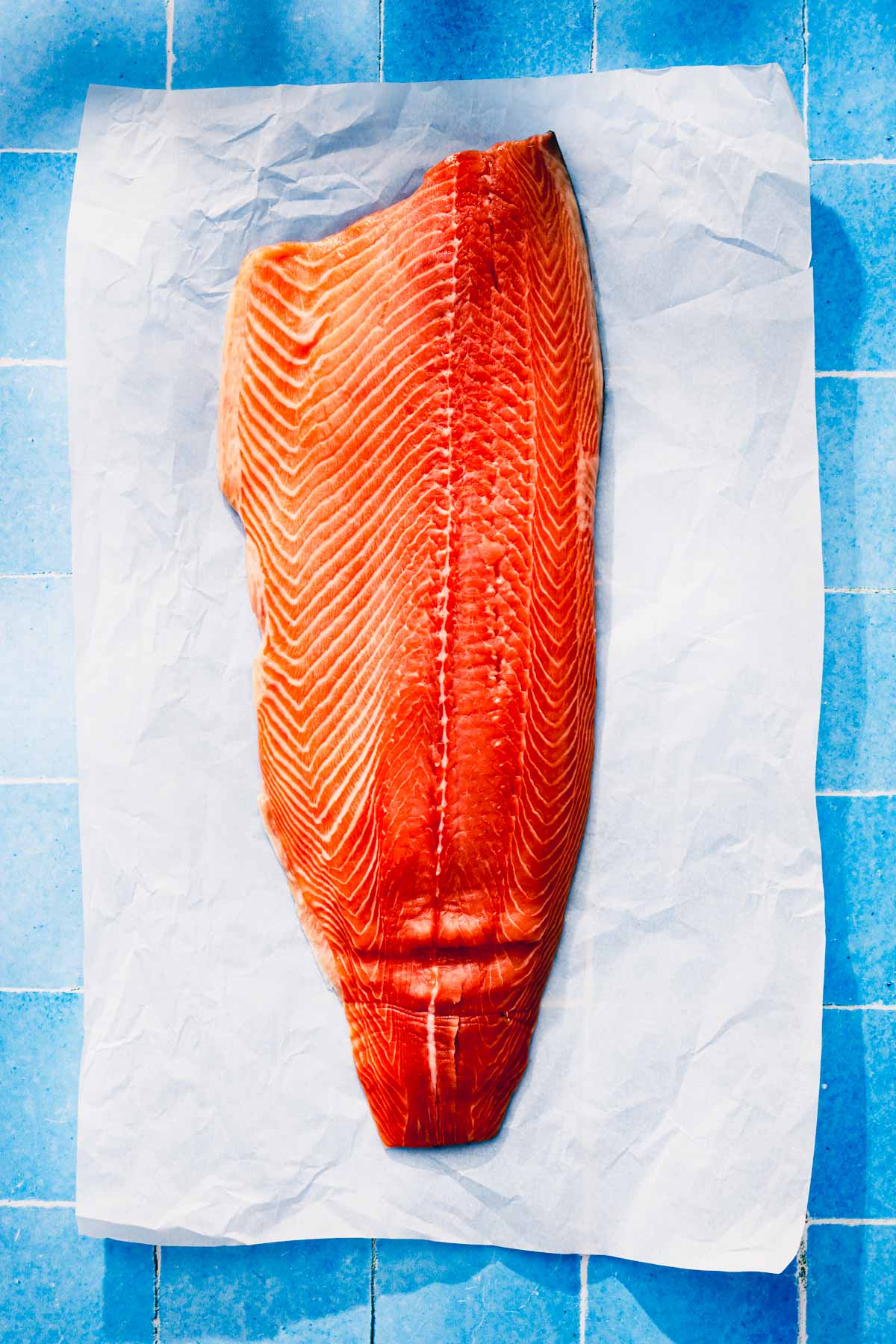 piece of raw salmon on parchment paper and blue tile