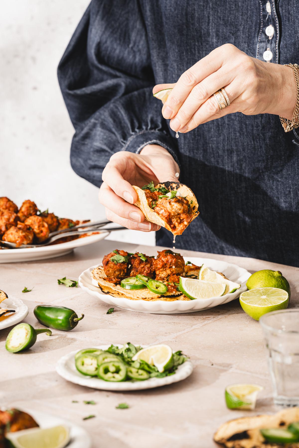 hands in frame holding tortilla with meatballs, other hand squezing a lime