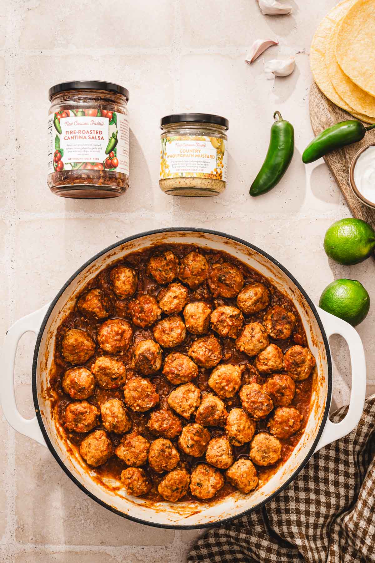 large skillet with meatballs cooked in the salsa sauce, jars with salsa and mustard