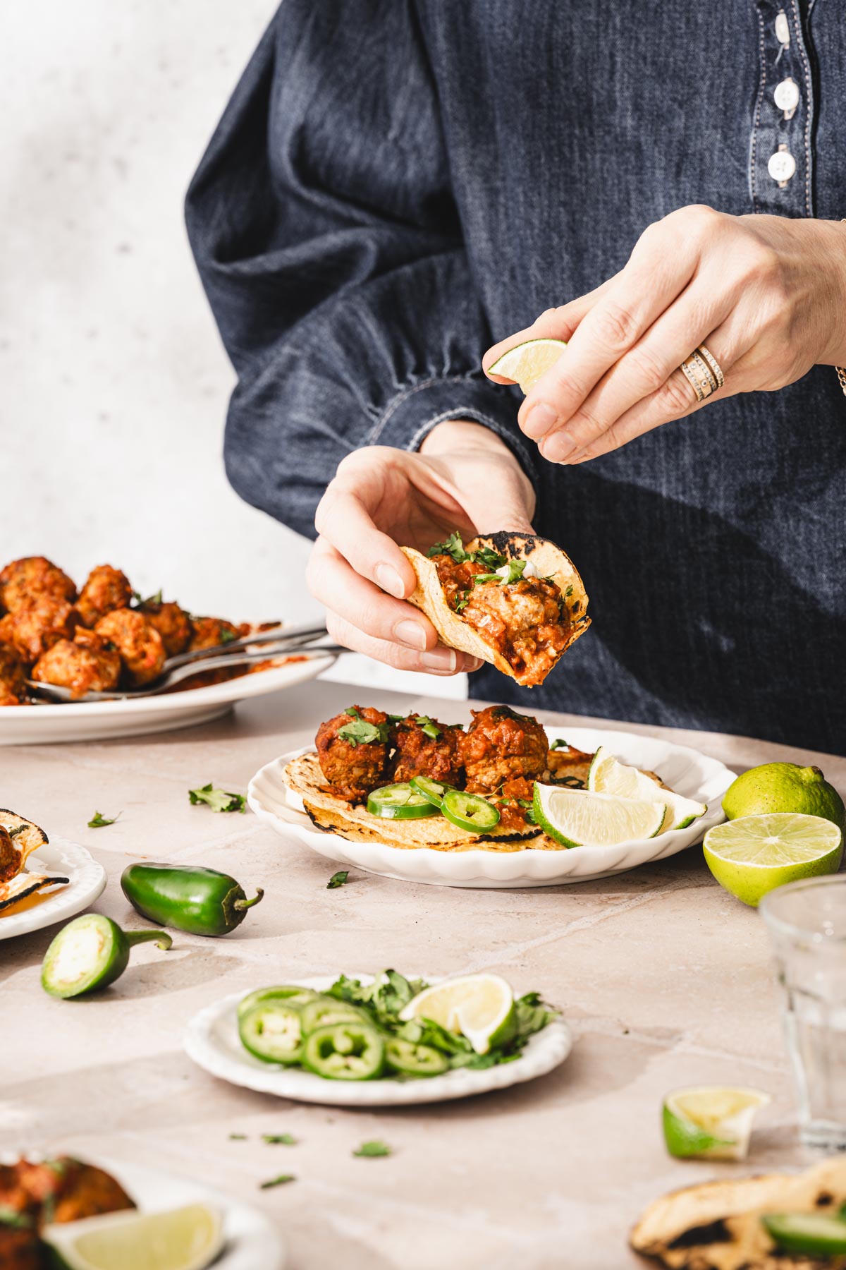 hands in frame holding tortilla with meatballs, other hand holding a lime