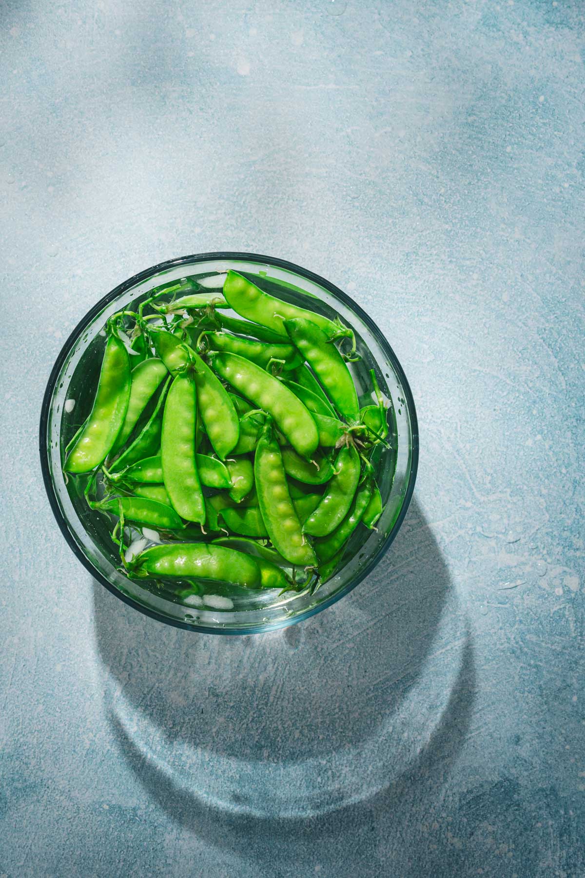 snow peas in a glass bowl filled with water and ice