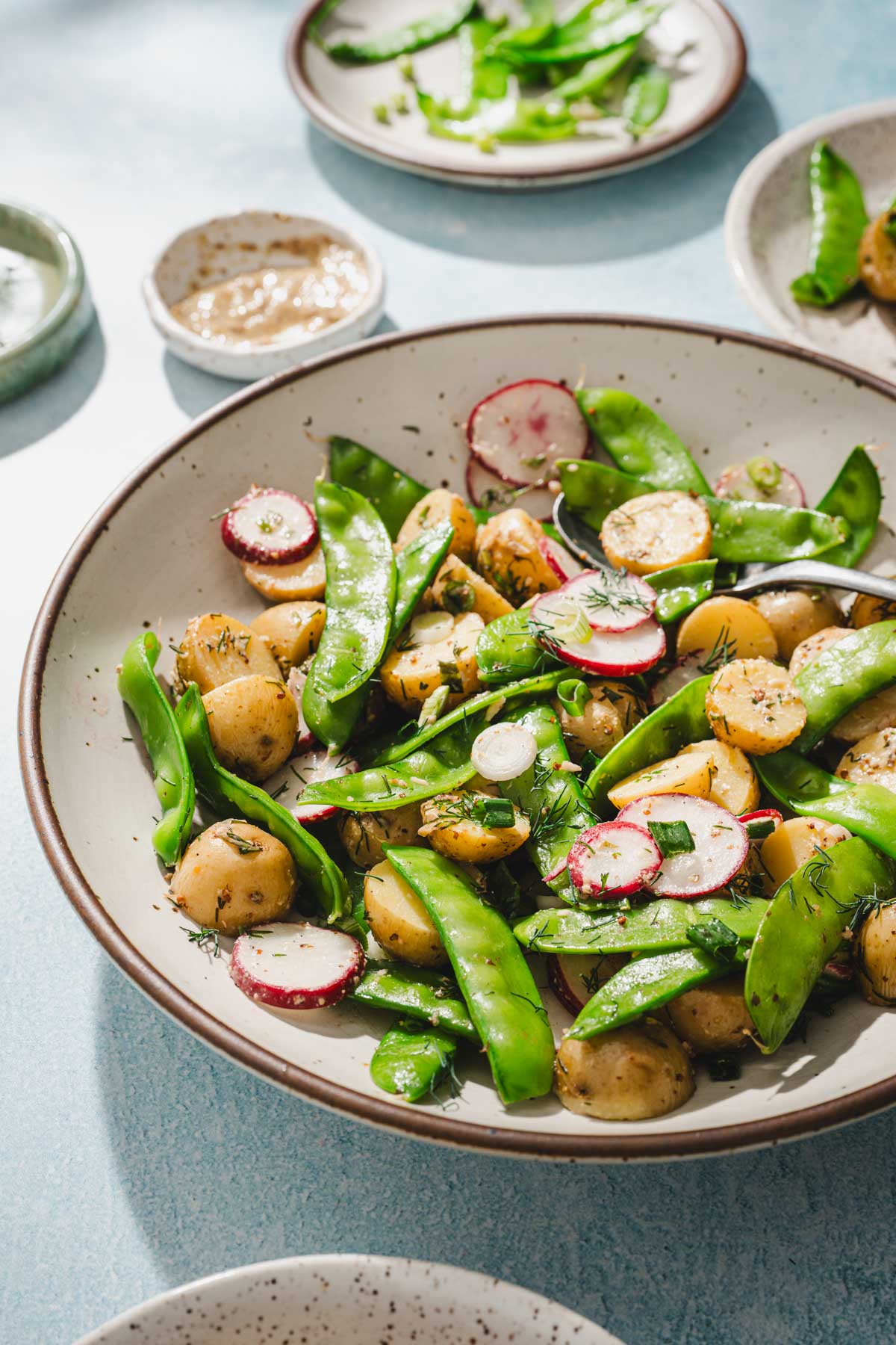 side view of a bowl with snow pea salad, other dishes around