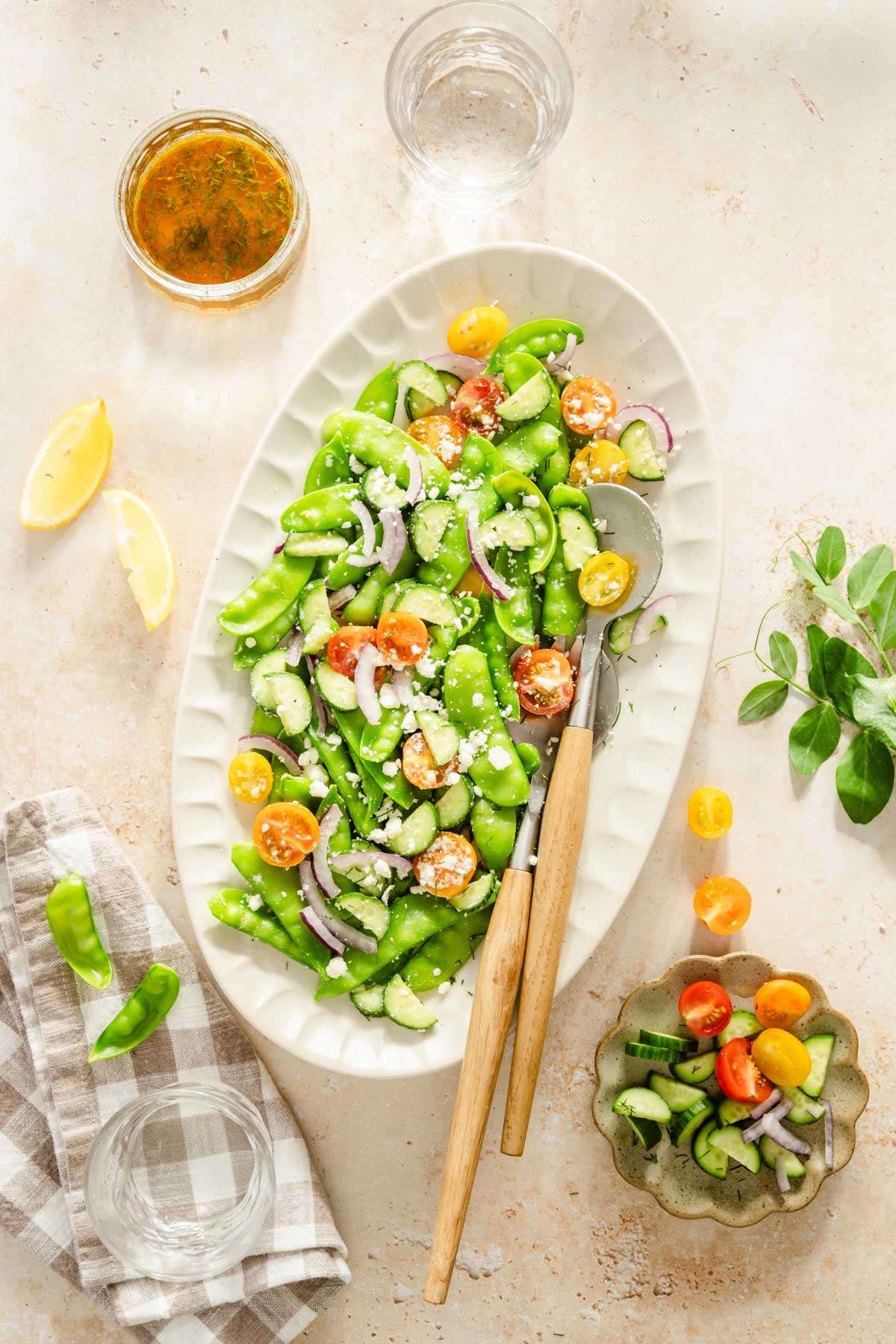 snow pea salad on a serving platter, serving utensils, dish with the dressing