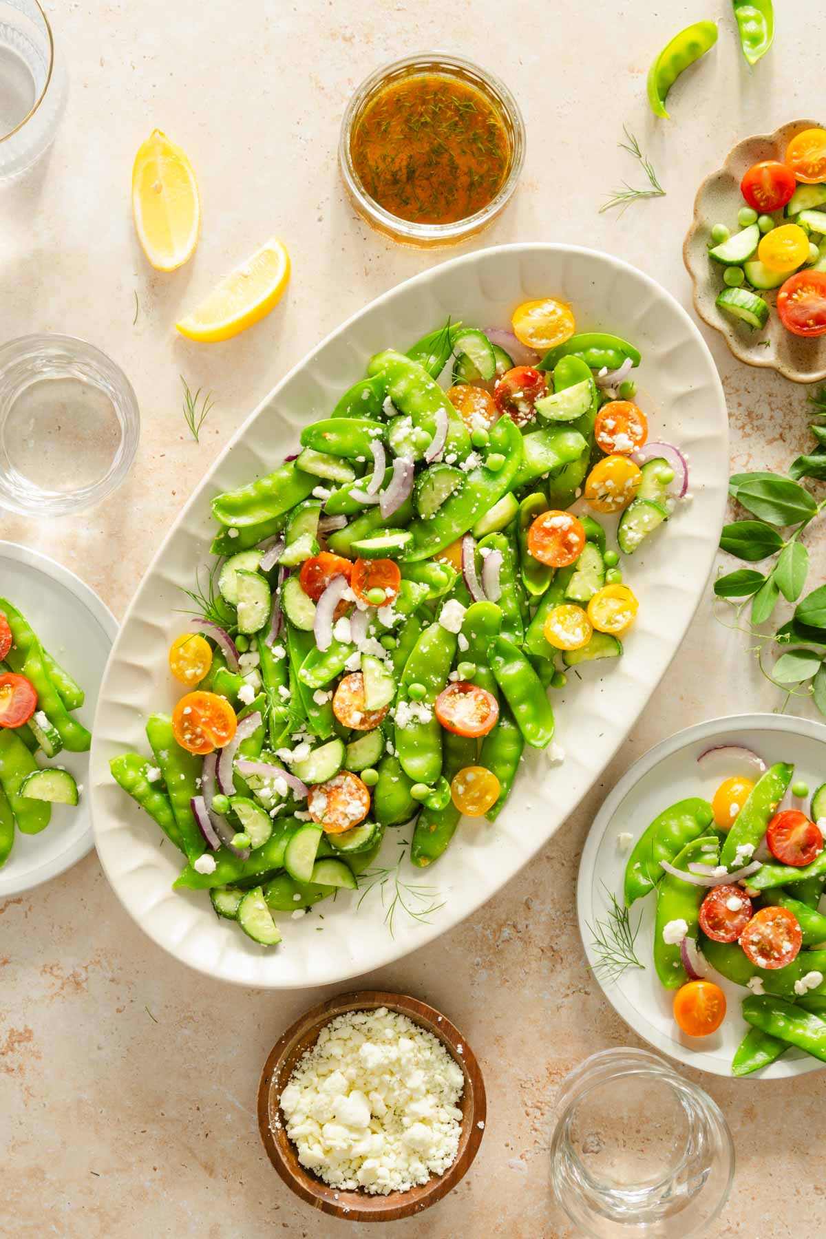 snow pea salad in a serving platter, few plates, dish with the dressing, lemon wedges, bowl with feta