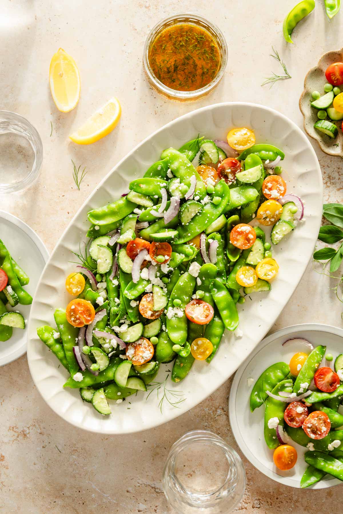 snow pea salad in a serving platter, few plates, dish with the dressing, lemon wedges, bowl with feta