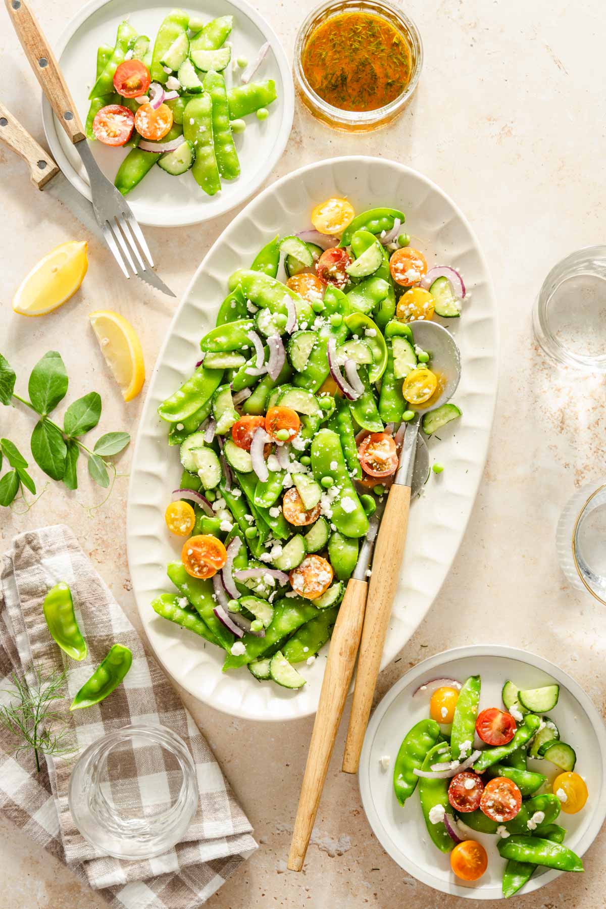 snow pea salad on a serving platter, napkin, serving utensils, few plates with the salad