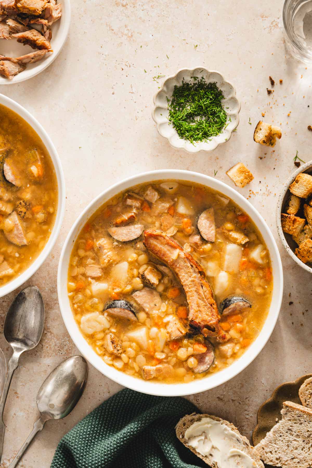 split pea soup in a serving bowls, dish with fresh dill, slices of bread, bowl with croutons