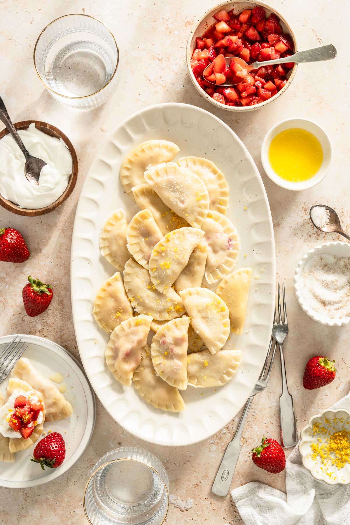 cooked pierogis on a serving platter, plate with few pierogis, small dishes with different toppings