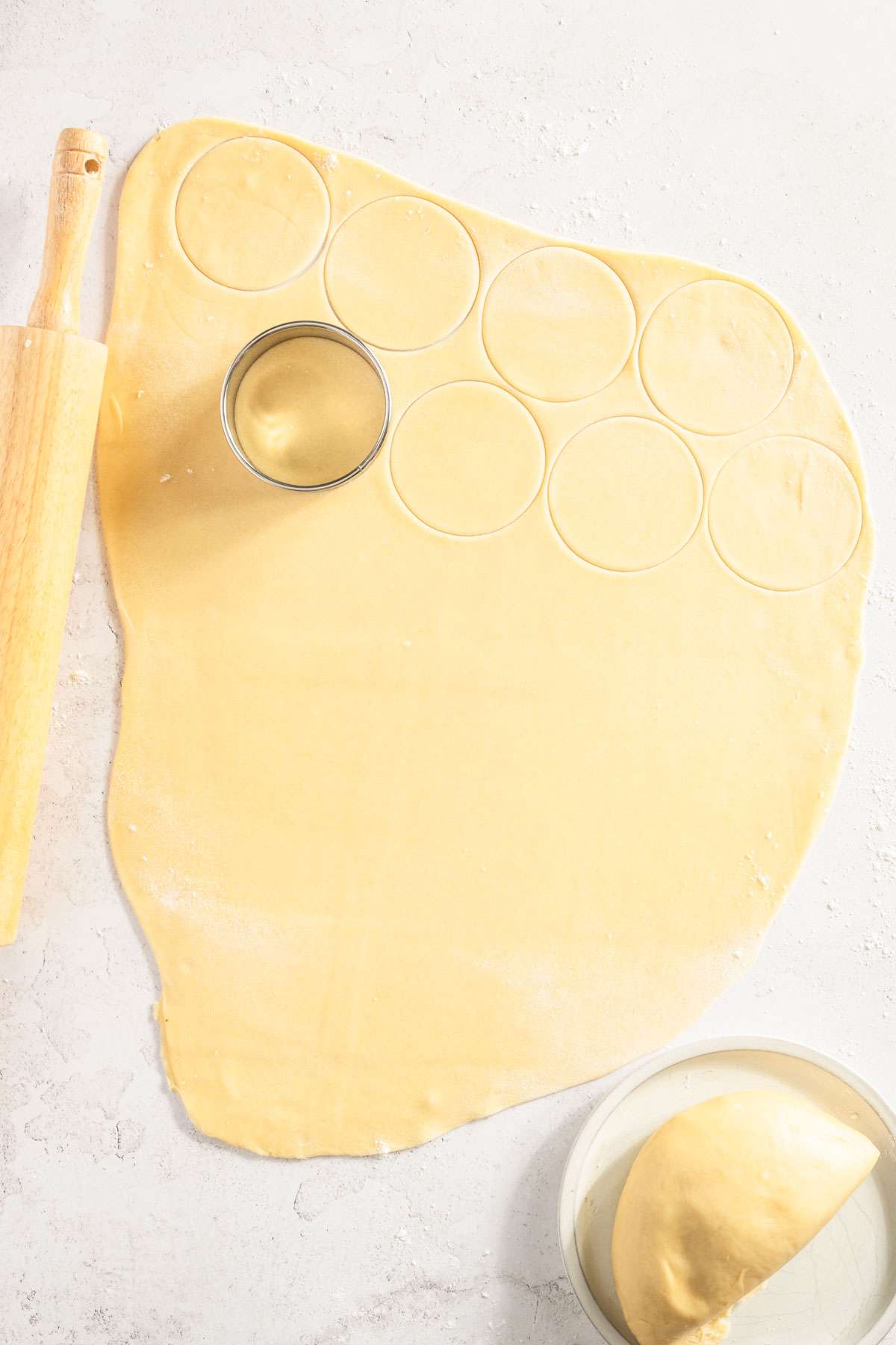 dough rolled out on a tables, rolling pin, cutting circle on top of the dough, some circles already cut out