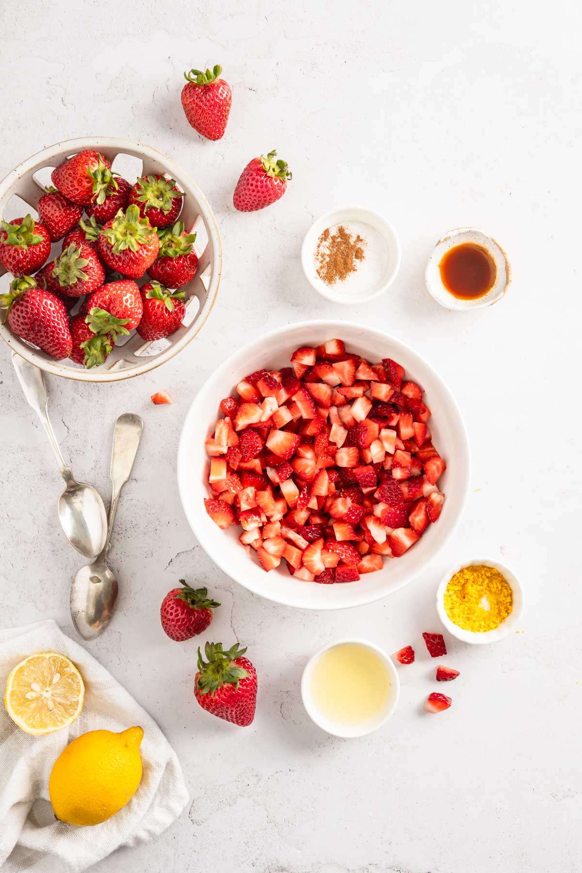 cut up strawberries in a mixing bowl, dish with whole berries, other ingredients around