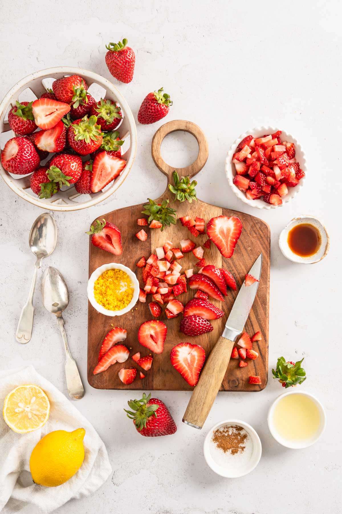 starwberries on acutting board, knife, spoons, emons around