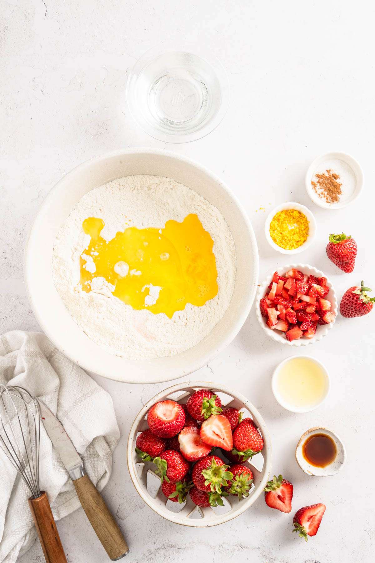 large mixing bowl with flour, egg and butter added in, other ingredients around