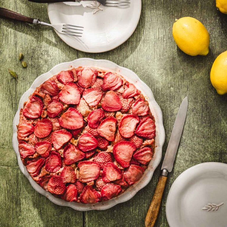 strawberry cake on a serving plate, lemons, small plates