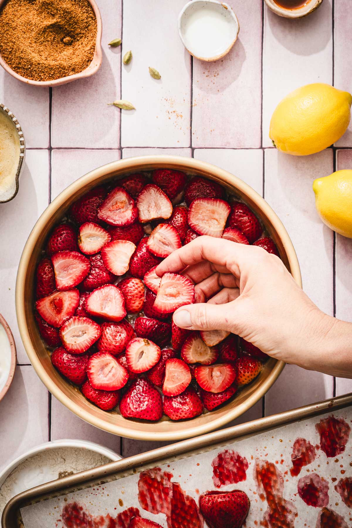 pan with strawberries arranged at the bottom, hand in frame holding a strawberry